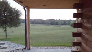 A covered porch with a view of a grassy field and trees.