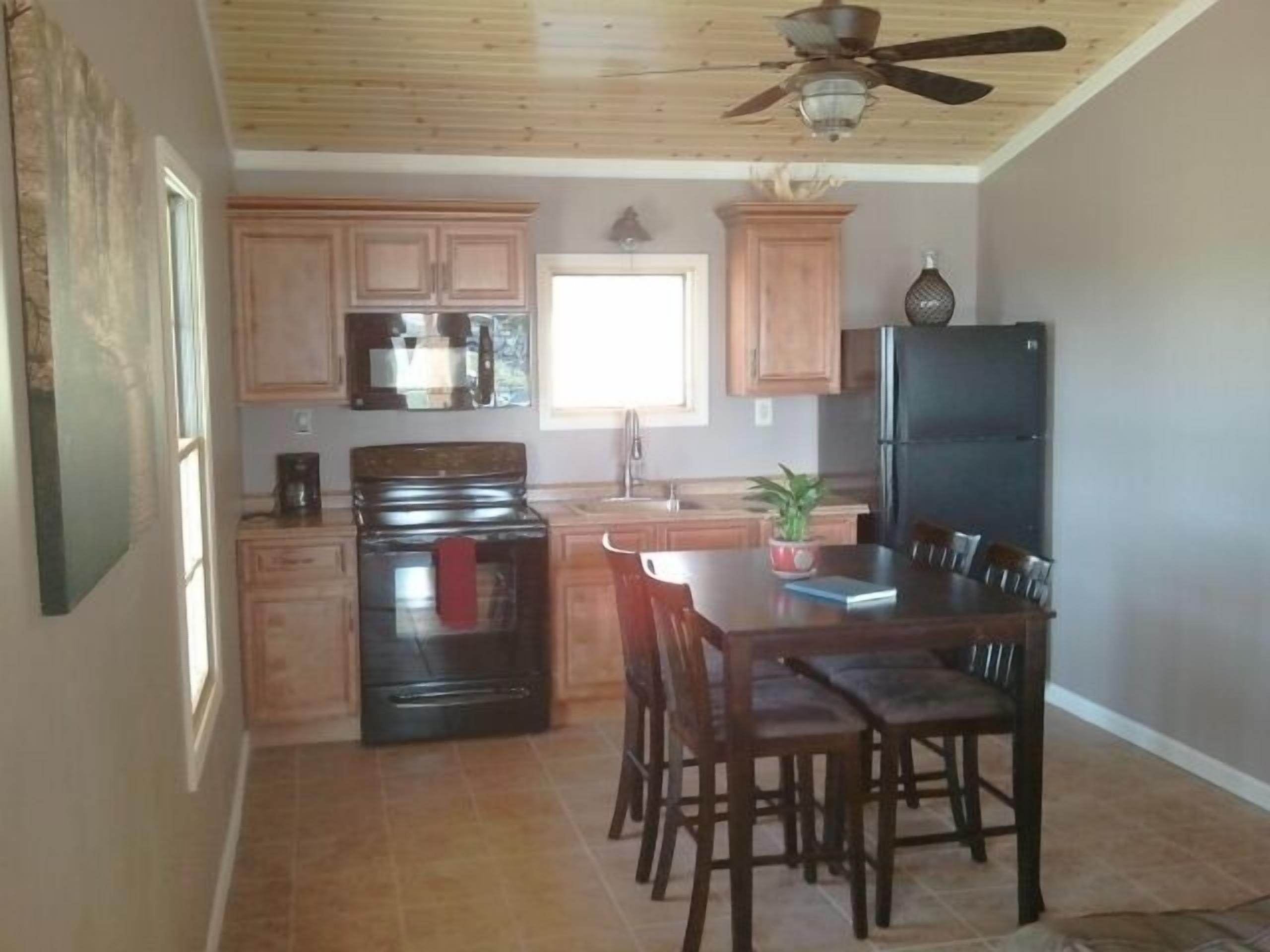A kitchen with wooden cabinets, a black stove, a refrigerator, and a dining table with chairs.