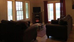 A living room with a fireplace, wooden ceiling, and large windows.