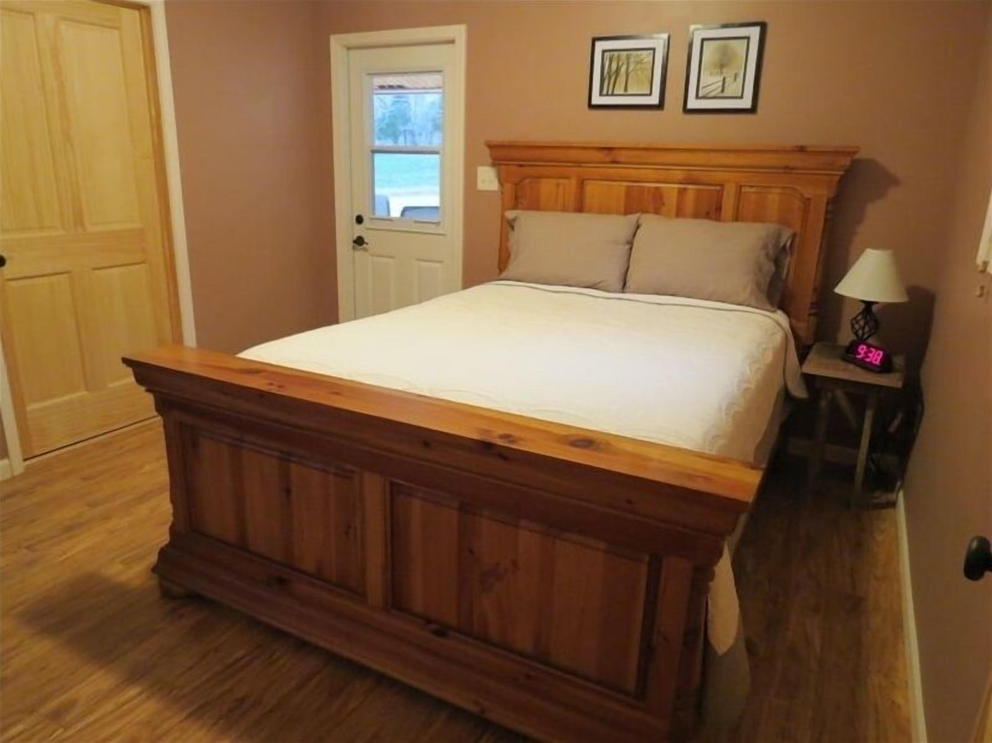 Un dormitorio con una cama de madera, una puerta y una mesita de noche con una lámpara.