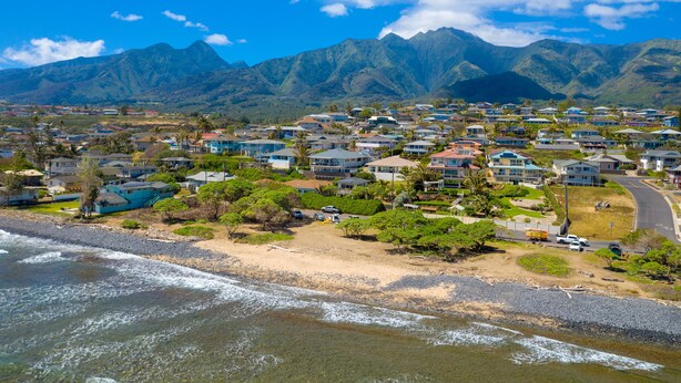 Zona residencial costera con casas, una playa y montañas al fondo.