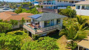 Una casa costera con balcón, paneles solares y abundante vegetación.