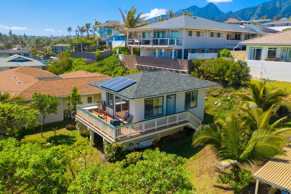 Una casa vista mare con balcone, pannelli solari e vegetazione rigogliosa.