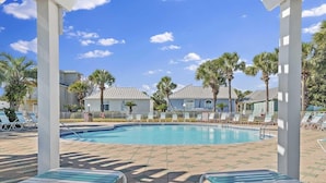 A pool area with lounge chairs, palm trees, and a building with a light-colored roof. - Charming, Pet Friendly Maravilla Cottage ~ Sleeps 8 ~ Beach Service Included (Destin)
