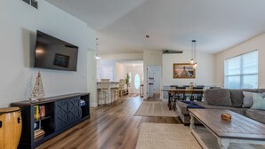 A modern living room with a flat-screen TV, a wooden coffee table, a sofa, and a dining area with a table and chairs. - Charming, Pet Friendly Maravilla Cottage ~ Sleeps 8 ~ Beach Service Included (Destin)