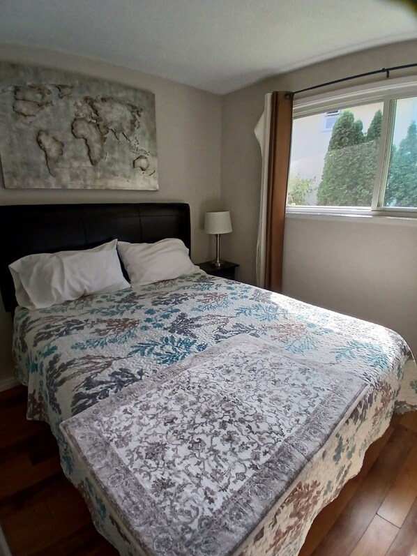 Une chambre à coucher avec un lit, une table de chevet, une lampe, une fenêtre avec des rideaux et une carte du monde accrochée au mur.