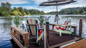 A dock with two Adirondack chairs, one with a striped cushion and another with a red cushion, and a large striped umbrella. - A lakefront playground near beautiful Victoria on British Columbia's west coast. (victoria)