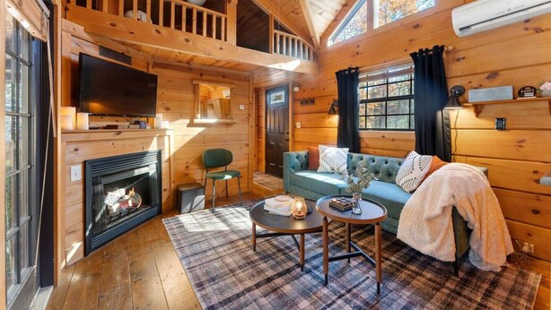Interno di una baita di legno con camino, televisione, divano e zona pranzo.