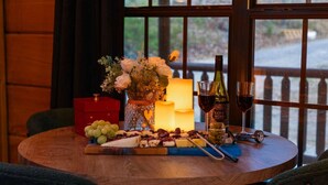Un tavolo rotondo in legno con una candela, una bottiglia di vino, bicchieri e un tagliere con formaggio.