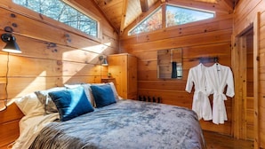 Camera da letto in una baita di legno, con un letto, cuscini, una lampada, uno specchio e un accappatoio appeso al muro.