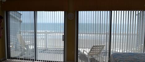 Una habitación con cama, una silla y vista a la playa a través de amplios ventanales correderos.