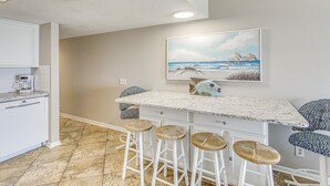A kitchen with white cabinets, a marble countertop, and three wicker stools. - Spectacular 3 BR/3BA Oceanfront Condo -2 Large Balconies- Best Views-Aug wks ! (North Myrtle Beach)