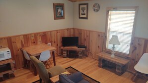 Una sala de estar acogedora con una mesa de comedor de madera, un sofá, un televisor y una ventana con persianas.