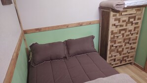 Una cama pequeña y ordenada con colchón y almohadas marrones, cabecera de madera y pared verde.