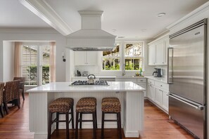 Una cocina moderna con una isla central, taburetes de bar, armarios blancos y un refrigerador de acero inoxidable.