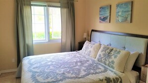 Un dormitorio con una cama grande, una mesita de noche, un ventanal con cortinas y dos obras de arte en la pared.