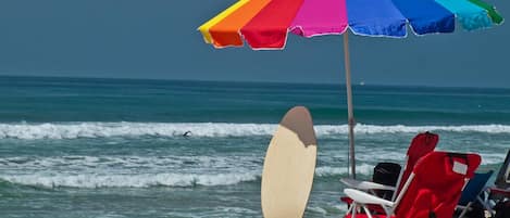 A beach with a colorful umbrella, a surfboard, and beach chairs.