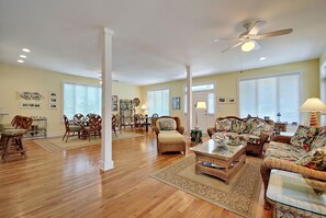 A spacious living room with hardwood floors, a dining area with wooden chairs, a large sofa set, and a ceiling fan.