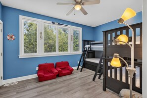 A room with blue walls, a bunk bed, a ceiling fan, and a window with blinds. - CLASSIC and Cozy IOP Beach Home, Family-Friendly, Walk to Marina! (Isle Of Palms)