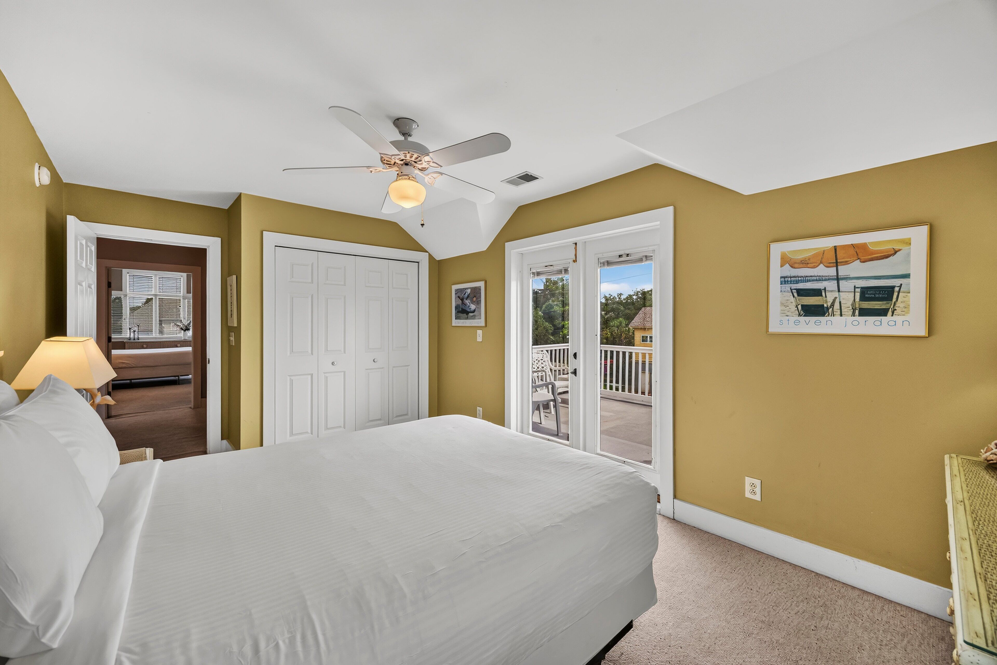 A bedroom with a bed, a ceiling fan, and a door leading to a balcony.