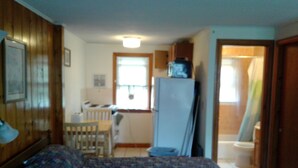 A bedroom with a bed, a small kitchenette, and a bathroom. - Dennisport - Studio Condo w kitchenette  - Walk to beach  (Dennis)