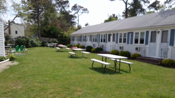 A grassy area with picnic tables and a building with a row of windows. - Dennisport - Studio Condo w kitchenette  - Walk to beach  (Dennis)