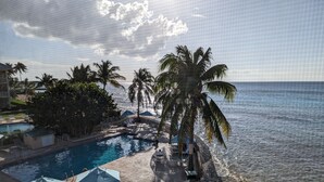A pool area with lounge chairs and umbrellas, palm trees, and a view of the ocean. - OCEAN FRONT, 7M BEACH, PLANTATION VILLAGE #28 (George Town)