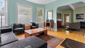 A spacious living room with a large window, a ceiling fan, and a coffee table. - Victorian With An Amazing Location, Incredible Yard With Private outdoor Hot tub (Minneapolis)