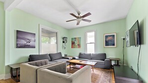A living room with a ceiling fan, two sofas, a coffee table, a TV, and artwork on the walls. - Victorian With An Amazing Location, Incredible Yard With Private outdoor Hot tub (Minneapolis)
