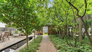 A brick pathway flanked by lush greenery and trees, leading to a seating area with chairs and a table. - Victorian With An Amazing Location, Incredible Yard With Private outdoor Hot tub (Minneapolis)