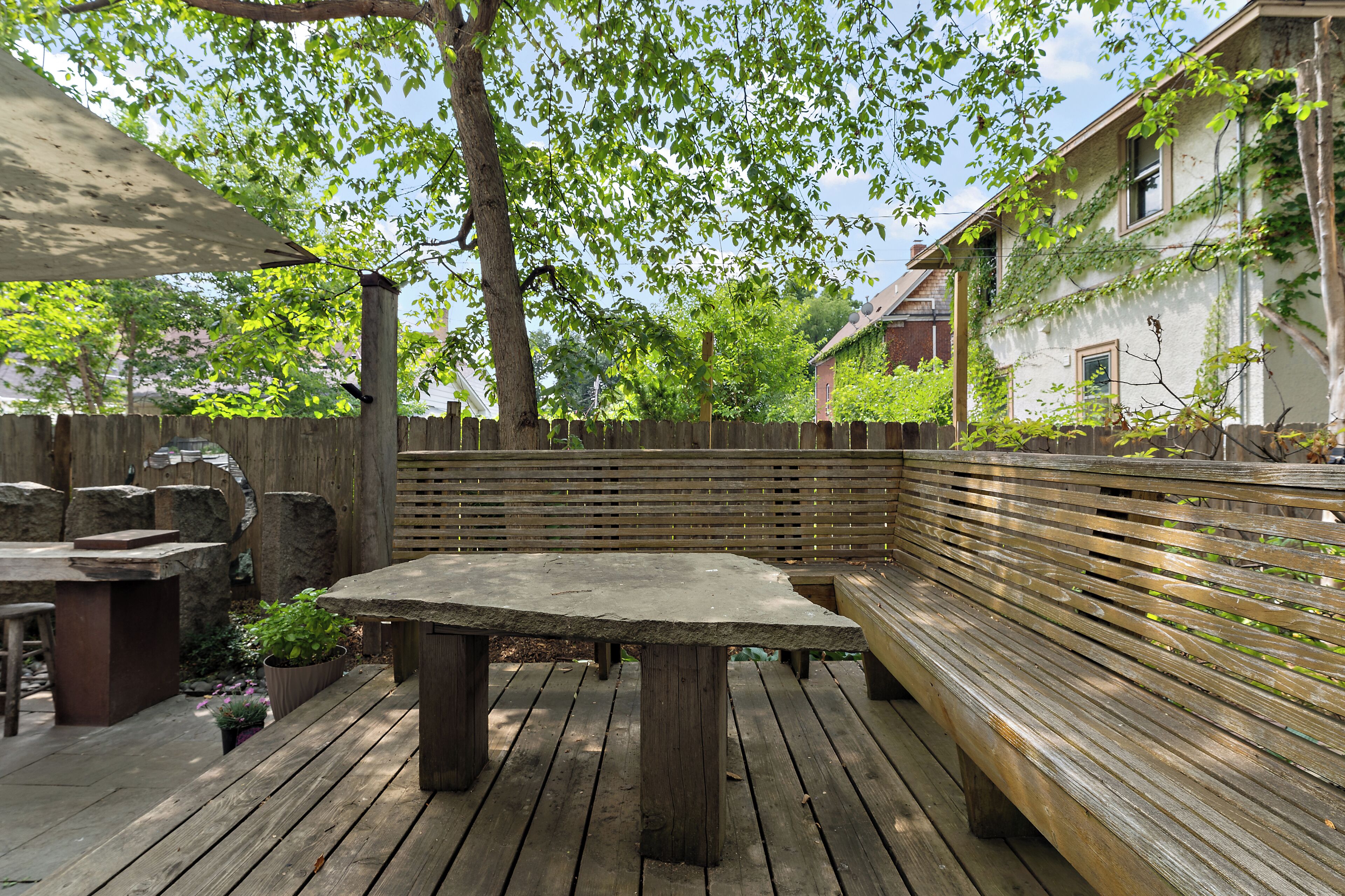 Un patio al aire libre con mesa y banco de madera, rodeado de un cerco de madera y follaje.