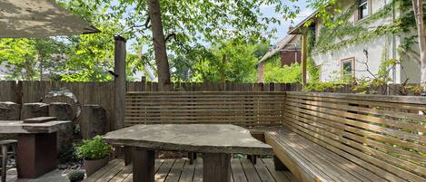 Un patio al aire libre con mesa y banco de madera, rodeado de un cerco de madera y follaje.