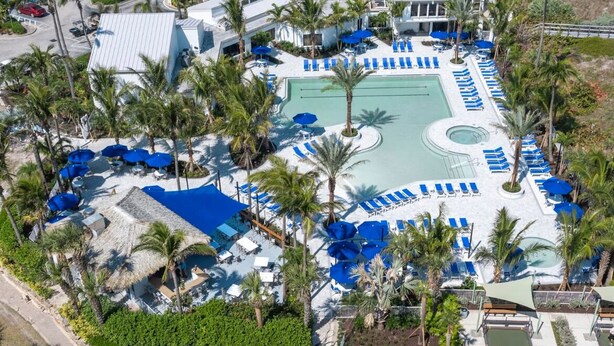 An aerial view of a resort with a central swimming pool, multiple lounge areas with blue umbrellas, and palm trees. - Beautiful Ocean Village -  On Hole One of the lower floor of the golf course (Fort Pieerce)