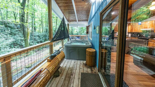 Un terrazzo in legno con una vasca idromassaggio, una panchina di legno e una porta in vetro che dà su un'area cucina.
