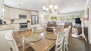 A spacious kitchen with white cabinetry, stainless steel appliances, and a dining area with a wooden table and white chairs. - Private Pool, 2 Blocks to Beach--Perfect Family Getaway! (Isle of Palms)