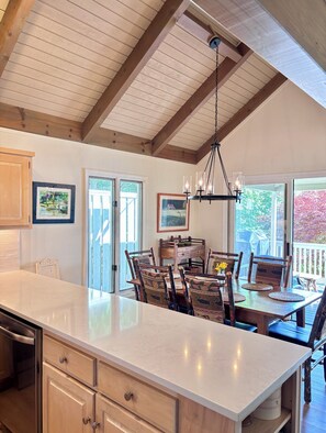 A kitchen with a large island, wooden ceiling beams, and a dining area with chairs and a table.