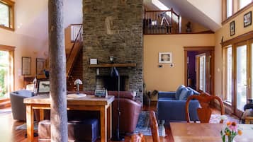 A spacious living room with a stone fireplace, wooden furniture, and large windows.