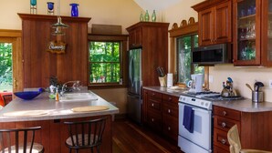 Une cuisine avec des meubles en bois, un réfrigérateur en acier inoxydable, un four à micro-ondes et une cuisinière. On y trouve deux tabourets de bar et une fenêtre donnant sur les arbres.