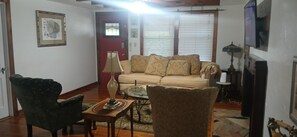 A living room with a sofa, two chairs, a coffee table, a lamp, and a door with a window.