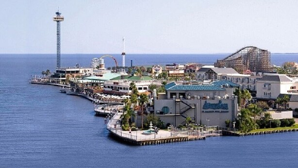 Ein Küstenhotel mit einer an das Wasser führenden Mole, einem Leuchtturm und einer Achterbahn.