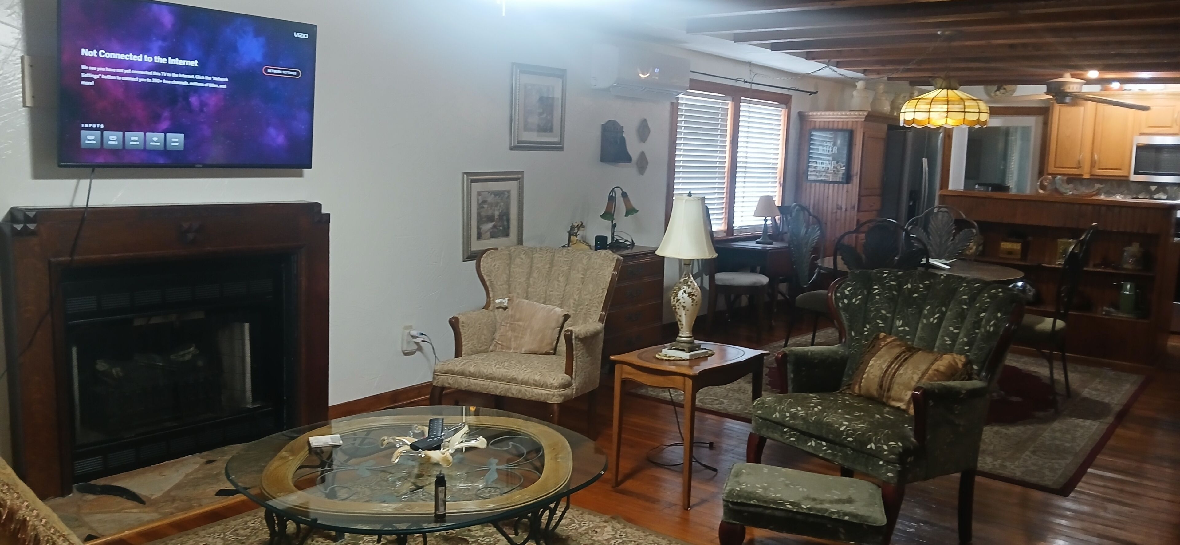 A living room with a fireplace, a television displaying a 'Not Connected to the Internet' message, and a dining area with wooden cabinets and a chandelier.