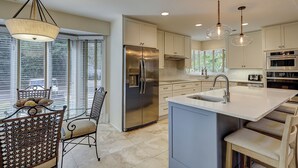 A modern kitchen with a large island, stainless steel appliances, and a dining area with wicker chairs. - 3rdRowOcean Palmetto Dunes Dog Friendly Home w/ FREE Pool/Spa Heat Seasonally (Hilton Head Island)