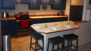 Een moderne keuken met donkerblauwe kastjes, een roestvrijstalen fornuis en een centraal kookeiland met krukken.