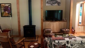 Een gezellige woonkamer met een houtkachel, een televisie, houten meubels en een groot raam.
