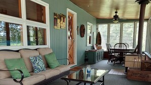 A cozy room with a green wall, a wooden ceiling, a sofa with green cushions, a glass table, and a dining area with chairs and a table.