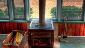 A wood-burning stove in a room with large windows, a wooden bench, and a box of books.