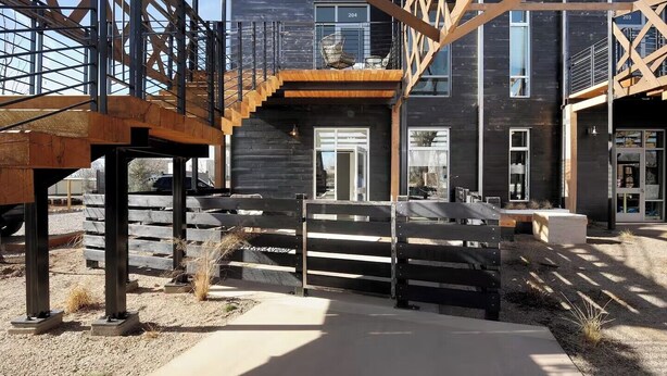 A modern building with a wooden staircase leading to a balcony, a metal railing, and a concrete pathway. - Sunny Chic Baca Railyard Retreat: Balcony + Full Kitchen + Laundry (Santa Fe)
