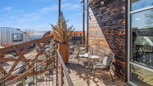 A wooden deck with outdoor seating, a large planter, and a view of a modern building. - Sunny Chic Baca Railyard Retreat: Balcony + Full Kitchen + Laundry (Santa Fe)