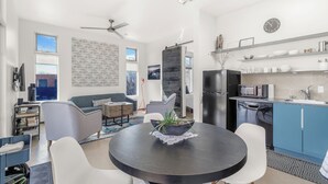 A modern living room with a round dining table, grey sofa, and a ceiling fan. - Sunny Chic Baca Railyard Retreat: Balcony + Full Kitchen + Laundry (Santa Fe)