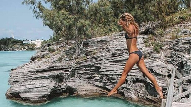 Una persona caminando sobre una cornisa rocosa junto al agua.